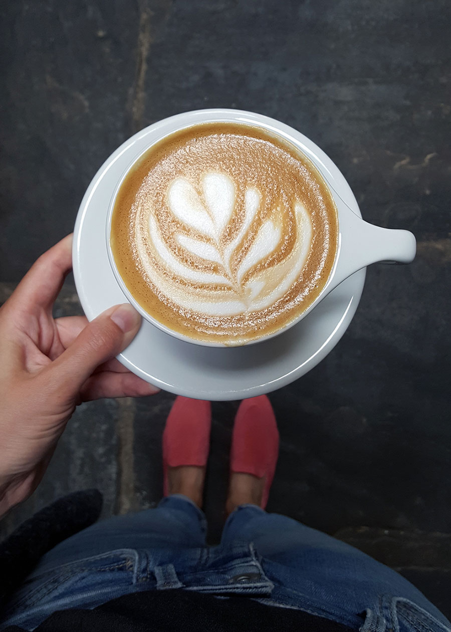 Eine Hand hält eine Tasse Kaffee mit perfekter Latte Art