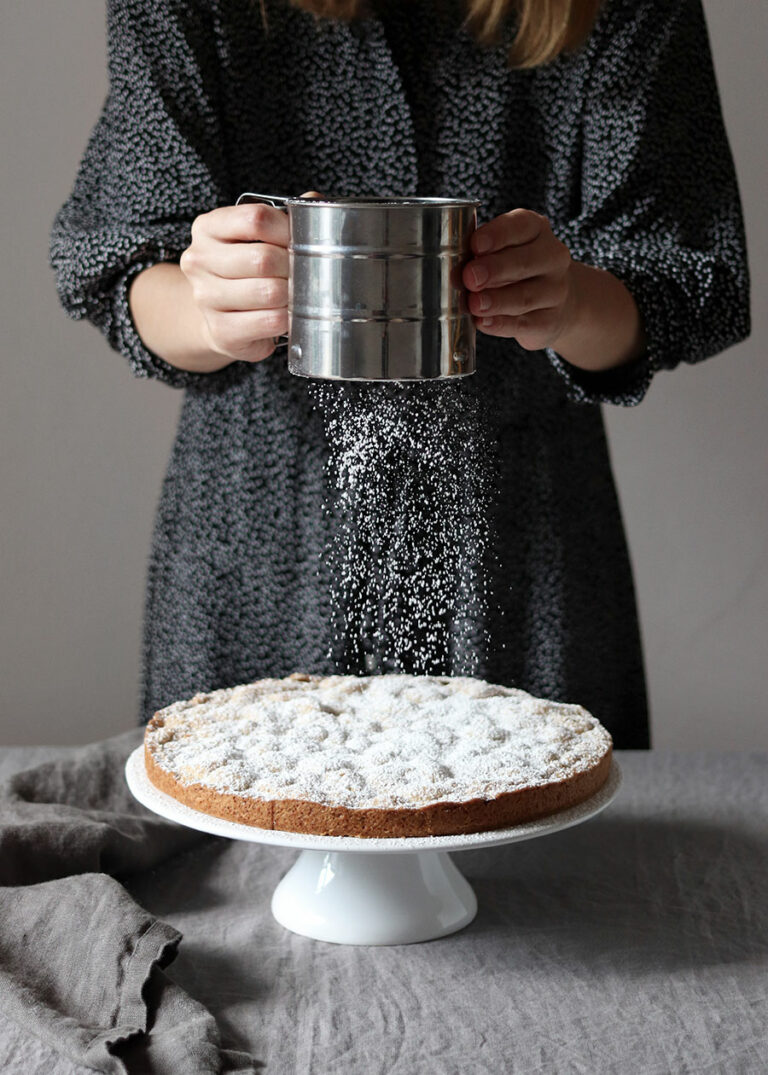 Foodfotografie - Frau streut Puderzucker über einen Kuchen