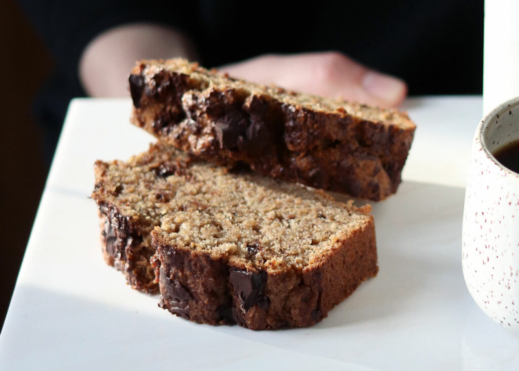 Zwei Scheiben Banana Bread liegen auf einer hellen Platte