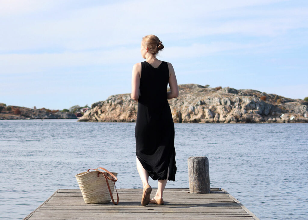 Eine Frau steht am Steg mit Blick auf eine felsige Küstenlandschaft