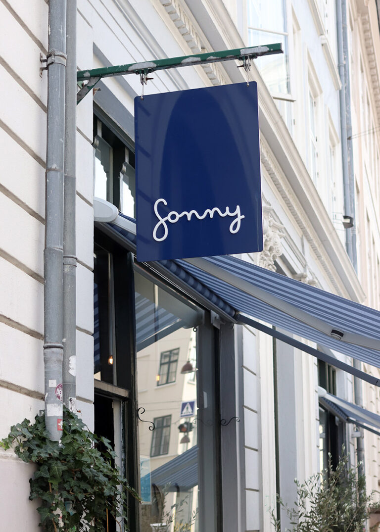 Ein blaues Schild mit dem Schriftzug Sonny markiert den Eingang zum Café